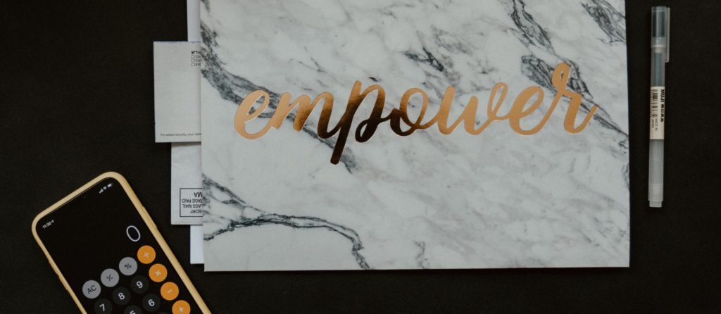 Kalligrafie Karte "Empower" auf einem schwarzen Schreibtisch mit einem Smartphone und Rechner